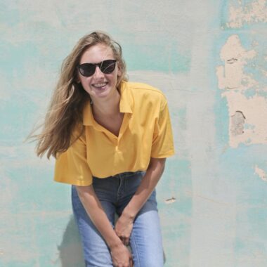 Woman Wearing Yellow Polo Shirt Standing in Front of Teal Concrete Wall