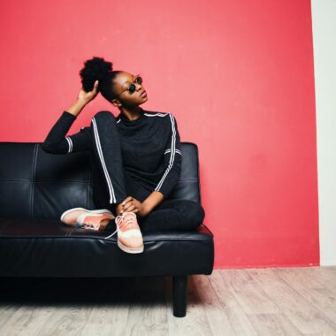 Woman With Black-and-white Sweater With Pants Sitting on Black Leather Sofa Beside Red Painted Wall